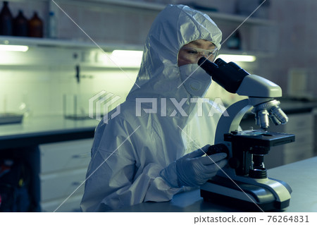 Chemist in protective workwear using microscope at work Chemist in protective workwear using microscope at work 76264831