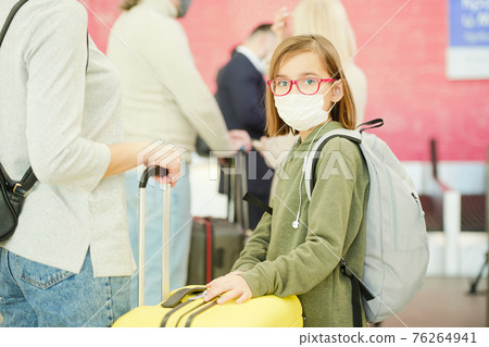 Little girl in casualwear, eyeglasses and protective mask standing against travelers in queue 76264941