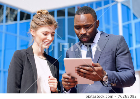 Young African businessman and his blond female colleague discussing points of presentation Young African businessman and his blond female colleague discussing points of presentation 76265082