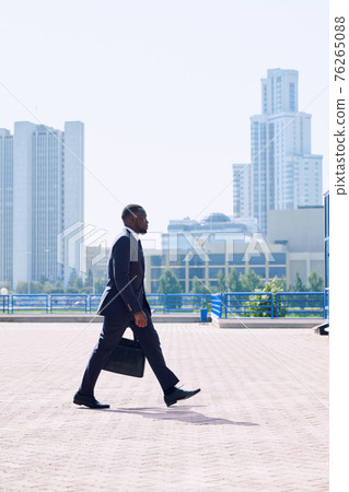 Young elegant African businessman in formalwear moving down sidewalk in front of camera Young elegant African businessman in formalwear moving down sidewalk in front of camera 76265088