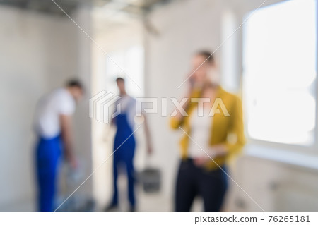 Blurred background of builders are renovating a room, a woman speaks on the phone Blurred background of builders are renovating a room, a woman speaks on the phone 76265181