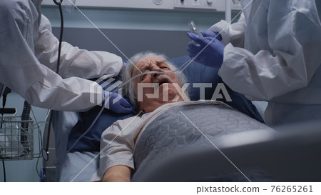 Doctors helping aged patient with breathing problems 76265261