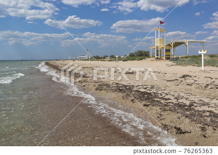 Rescue tower with a red flag on the empty beach of the resort village Vitino 76265363