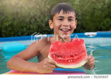 happy wet boy being in the pool holding a piece of watermelon and laughing, summer and vacation concept happy wet boy being in the pool holding a piece of watermelon and laughing, summer and vacation concept 76265607