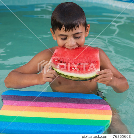 wet boy in the pool with a swimming board, bites a piece of watermelon, closing his eyes, summer vacation concept wet boy in the pool with a swimming board, bites a piece of watermelon, closing his eyes, summer vacation concept 76265608