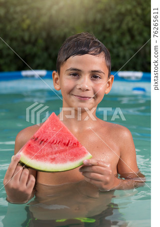 boy is in the pool, holds a slice of watermelon in his hands and smiles, summer concept boy is in the pool, holds a slice of watermelon in his hands and smiles, summer concept 76265611