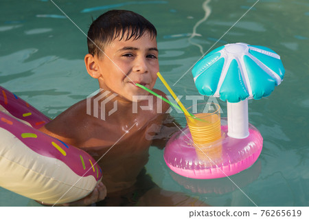 boy with a rubber ring and with a refreshing drink, swims in the pool, the concept of rest boy with a rubber ring and with a refreshing drink, swims in the pool, the concept of rest 76265619