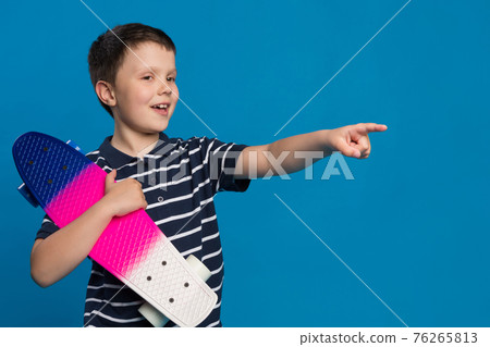 happy boy, teenager with a skateboard in his hand smiling, one hand pointing to the side, lifestyle happy boy, teenager with a skateboard in his hand smiling, one hand pointing to the side, lifestyle 76265813