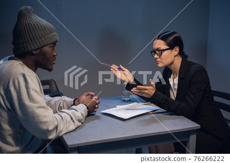 A lawyer girl with glasses and a young black guy communicate in the interrogation room about the grounds for his detention 76266222