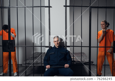 A strict prison guard in uniform guards cells with prisoners in a maximum security prison. 76266245