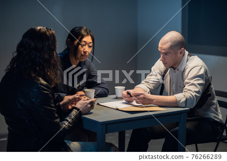At the police station, two officers are interrogating the captured criminal At the police station, two officers are interrogating the captured criminal 76266289
