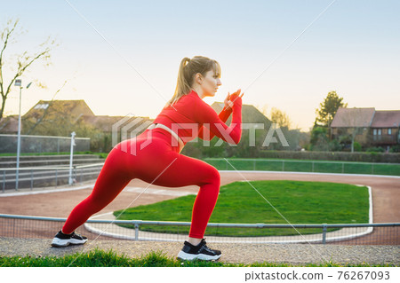 Back view Young fitness woman in red sport wear doing side lunge, squats during outdoors workout on the stadium steps. Stretching after running workout. Active lifestyle and health care. Copy space. Back view Young fitness woman in red sport wear doing side lunge, squats during outdoors workout on the stadium steps. Stretching after running workout. Active lifestyle and health care. Copy space. 76267093
