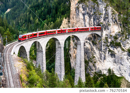 Passenger train crossing the Landwasser Viaduct in Switzerland 76270584