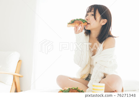 Woman eating bread on the bed 76271348