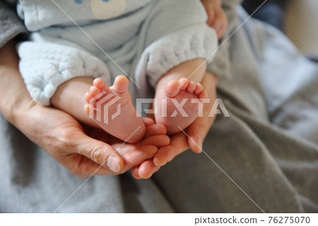 Up of both feet of the baby held by the mother 76275070