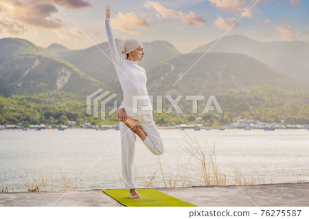 Kundalini yoga woman in white clothes and turban practices yoga kundalini on the background of the sea, mountains and sunset. Fighting face painting of the Indians shows her inner world. Visual Kundalini yoga woman in white clothes and turban practices yoga kundalini on the background of the sea, mountains and sunset. Fighting face painting of the Indians shows her inner world. Visual 76275587