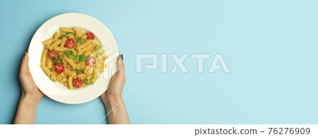 Pasta food on a blue banner background with female hands. Italian fusilli pasta with tomatoes and basil on a white plate. Pasta food on a blue banner background with female hands. Italian fusilli pasta with tomatoes and basil on a white plate. 76276909