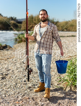 Happy fisherman with caught fish on a hook and a fishing rod in his hands 76277629