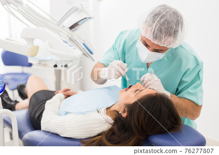 Dentist man examining a latin female patient teeth Dentist man examining a latin female patient teeth 76277807