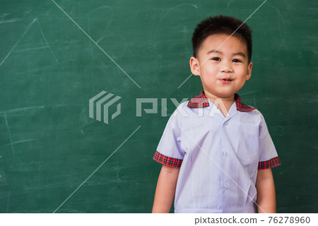 child from kindergarten in student uniform smiling on green school blackboard 76278960