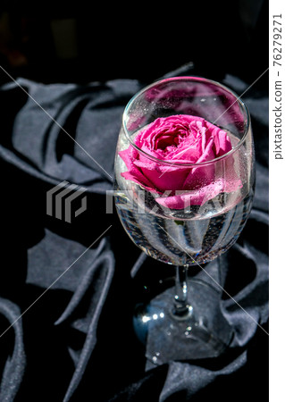Wine glass filled with pink flower petalson table with black silk fabric. Minimal modern still life. Holiday concept Valentines or womans day background design Wine glass filled with pink flower petalson table with black silk fabric. Minimal modern still life. Holiday concept Valentines or womans day background design 76279271
