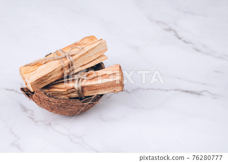 Palo Santo tree sticks inside coconut shell on light marble background - holy incense tree from Latin America. Meditation, mental health and personal fulfilment concept. Selective focus 76280777