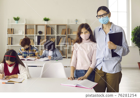 Portrait of female teacher and little schoolgirl in protective masks at school in class. 76281254
