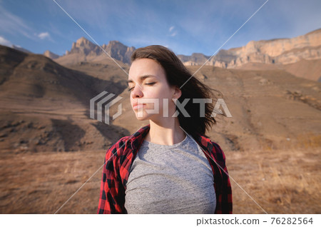young attractive woman stands in a shirt against a background of mountains young attractive woman stands in a shirt against a background of mountains 76282564