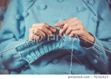 close up the woman's hands knitting a blue woolen sweater 76282625