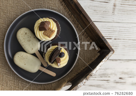 Muffins and cupcakes on tray. Cookie ice creams on a stick. Wooden background Muffins and cupcakes on tray. Cookie ice creams on a stick. Wooden background 76282680
