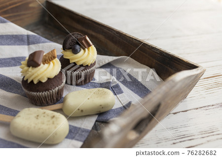 Muffins and cupcakes on tray. Cookie ice creams on a stick. Wooden background 76282682