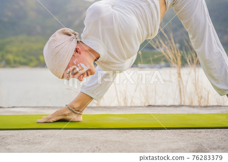 Kundalini yoga woman in white clothes and turban practices yoga kundalini on the background of the sea, mountains and sunset. Fighting face painting of the Indians shows her inner world. Visual Kundalini yoga woman in white clothes and turban practices yoga kundalini on the background of the sea, mountains and sunset. Fighting face painting of the Indians shows her inner world. Visual 76283379
