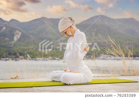 Kundalini yoga woman in white clothes and turban practices yoga kundalini on the background of the sea, mountains and sunset. Fighting face painting of the Indians shows her inner world. Visual Kundalini yoga woman in white clothes and turban practices yoga kundalini on the background of the sea, mountains and sunset. Fighting face painting of the Indians shows her inner world. Visual 76283389