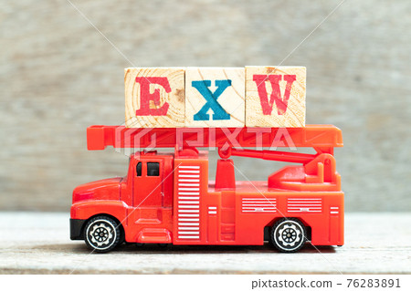 Fire ladder truck hold letter block in word EXW (abbreviation of Ex works) on wood background 76283891