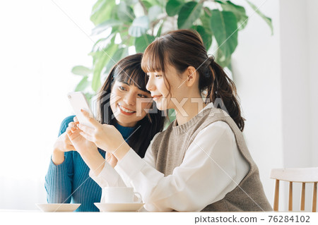 Two smiling women looking at a smartphone at a cafe Two smiling women looking at a smartphone at a cafe 76284102