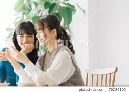 Two smiling women looking at a smartphone at a cafe Two smiling women looking at a smartphone at a cafe 76284103