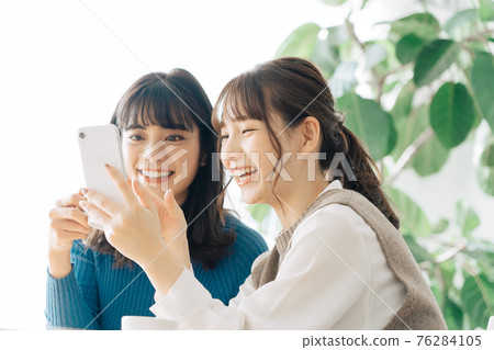 Two smiling women looking at a smartphone at a cafe 76284105
