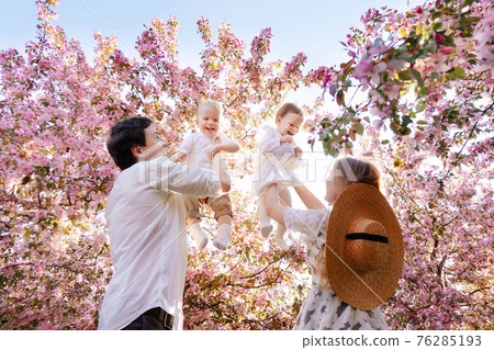 Parents with children play against the backdrop of greenery in the garden in summer. Parents with children play against the backdrop of greenery in the garden in summer. 76285193