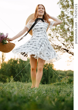 A young red-haired girl runs on the green grass in the summer picking flowers in a basket. A young red-haired girl runs on the green grass in the summer picking flowers in a basket. 76285221