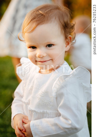 Portrait of a 2-year-old blonde daughter in a white cotton dress. Portrait of a 2-year-old blonde daughter in a white cotton dress. 76285233