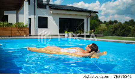 Young woman in swimming pool outdoors in backyard garden, relaxing. Young woman in swimming pool outdoors in backyard garden, relaxing. 76286541