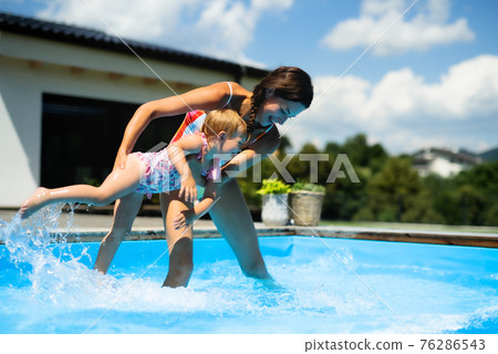 Mother with small daughter in swimming pool outdoors in backyard garden, playing. Mother with small daughter in swimming pool outdoors in backyard garden, playing. 76286543