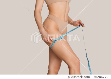 Beautiful female body in nude color underwear over grey background. Beautiful female body in nude color underwear over grey background. 76286779
