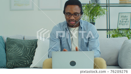 African-American businessman sit on sofa talk with client solve issues distantly through headphones. E-learn with e tutor, improve knowledge use videocall, modern tech concept. 76289276