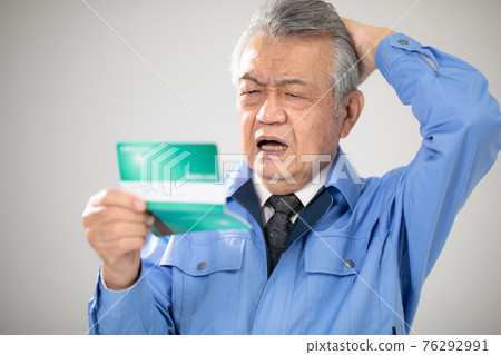 Senior man in work clothes looking at passbook Senior man in work clothes looking at passbook 76292991