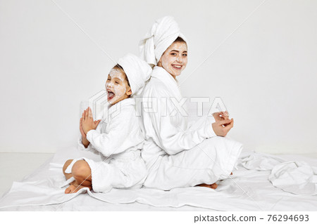 mother and daughter are sitting with towels on head and facial mask. 76294693
