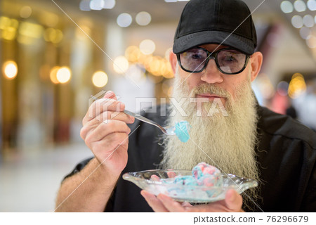 Close-up shot of man sitting in shopping mall and eating ice cream Close-up shot of man sitting in shopping mall and eating ice cream 76296679