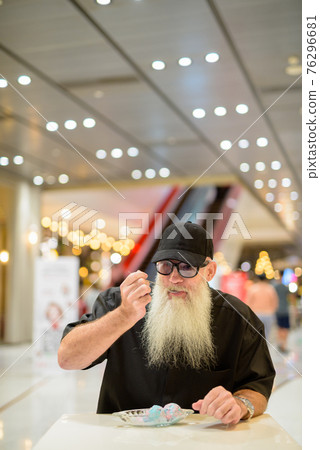 Vertical shot of man sitting in shopping mall and eating ice cream Vertical shot of man sitting in shopping mall and eating ice cream 76296681