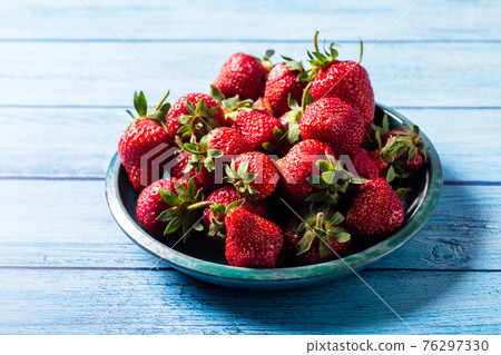 Fresh strawberries in green plate on blue wooden table 76297330