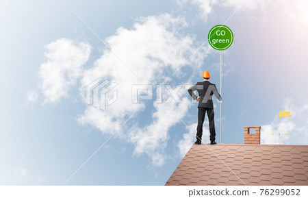 Businessman in suit on house top with ecology concept signboard. Mixed media Businessman in suit on house top with ecology concept signboard. Mixed media 76299052